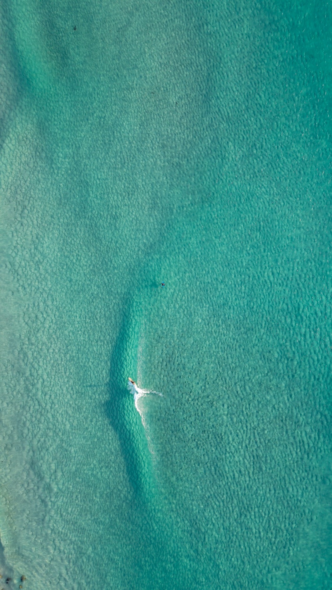 Lone surfer paddling across shallow reef