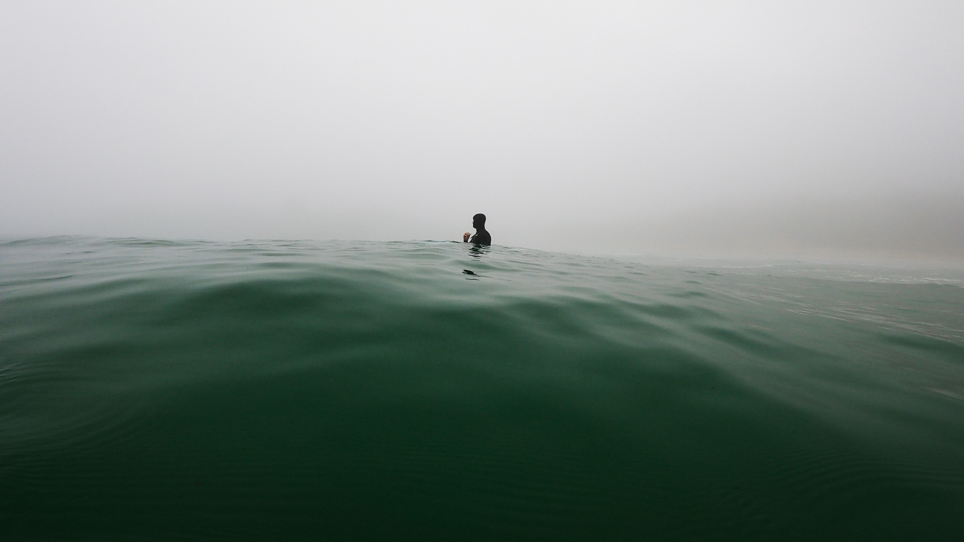 Surfer sitting in fog on a glassy sea