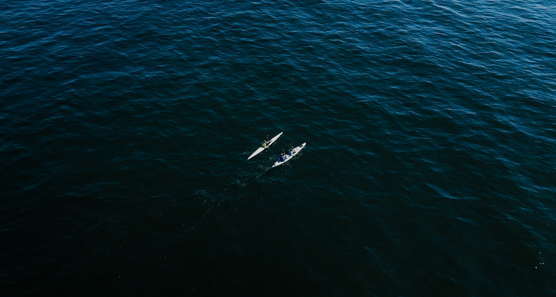 Two kayakers paddling across deep blue open ocean
