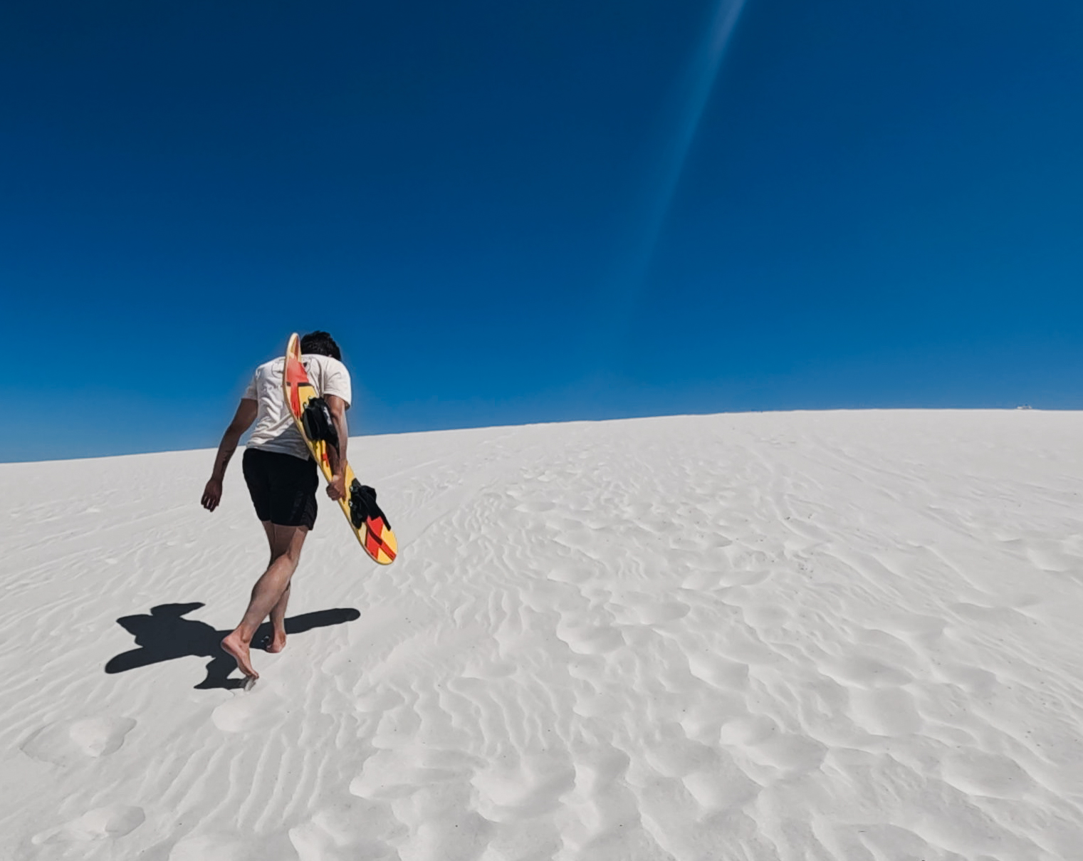 Sandboarding on white dunes under deep blue sky