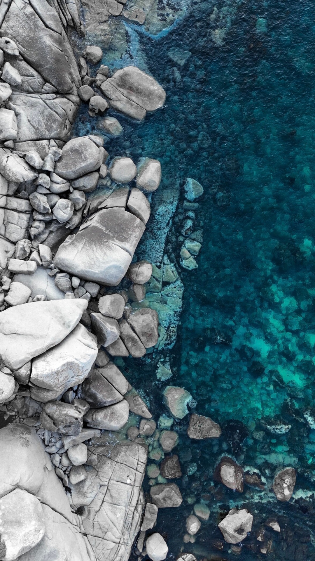 Aerial of grey rocks meeting turquoise water